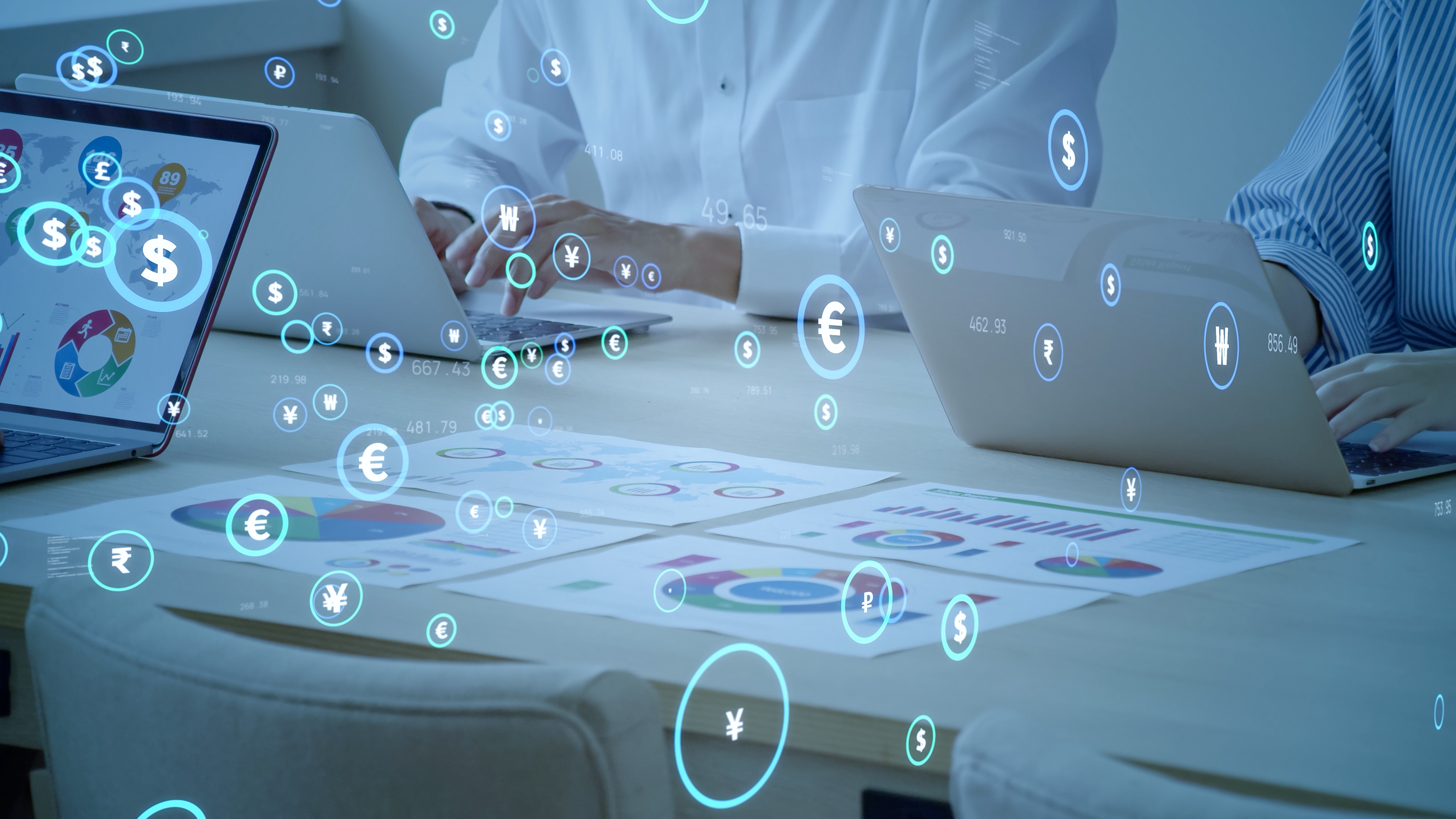 someone works on an open laptop. Only their hands are visible. On top of this photographic image are icons of different types of currency.