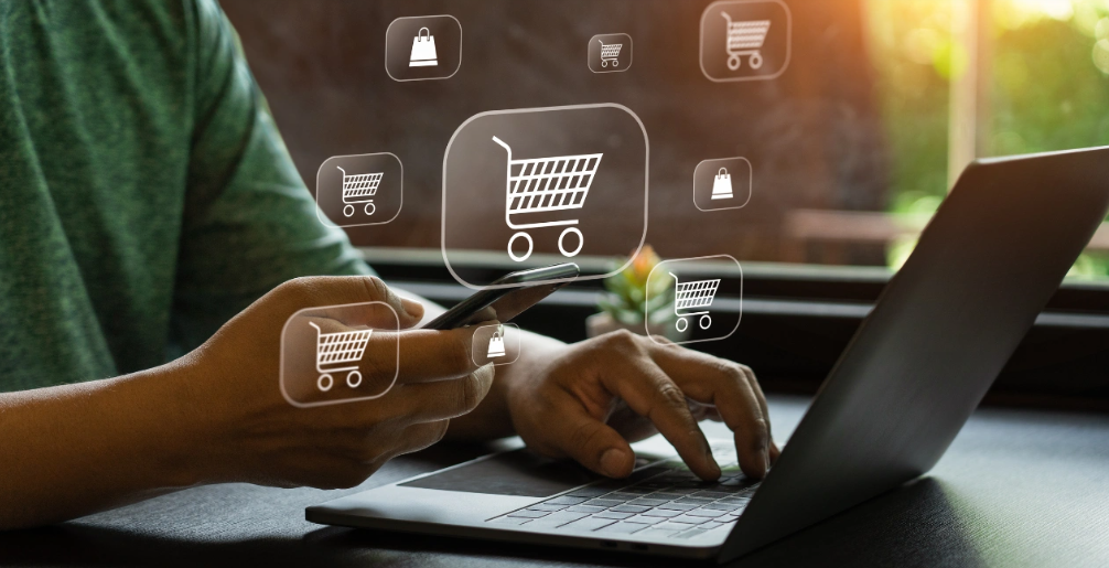 a photo pf hands above a laptop keyboard. On top graphics pf shoppingicons have been placed such as a shopping cart to suggest ecommerce