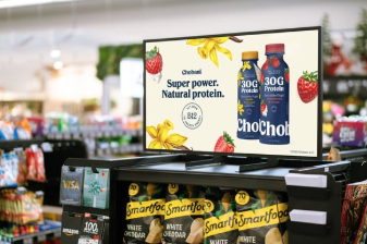 An image of a grocery store aisle. On top of the shelf is a digital screen showing an advert for juice