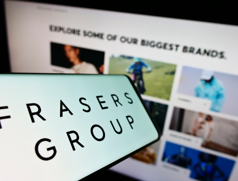 a photo of a phone with the Frasers Group logo on it in front of a computer screen showing a selection of images which represent their brands.