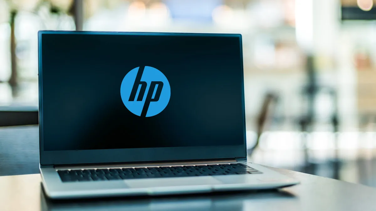 Laptop on a desk displaying blue Hewlett Packard logo, background is blurred.