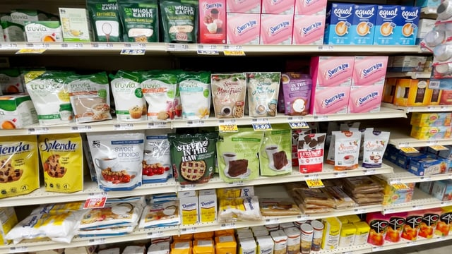 The image features a shelf stocked with various food items, including equal and Splenda. It is set in a convenience store or supermarket, highlighting the retail environment. The scene captures the organization of food storage within an indoor shop or pantry setting.