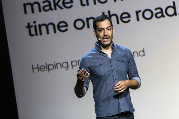The image features a man wearing a blue shirt. He engaged in an public speaking and presenting, and educating others in a professional setting. The context suggests he is focused on his role as an orator.