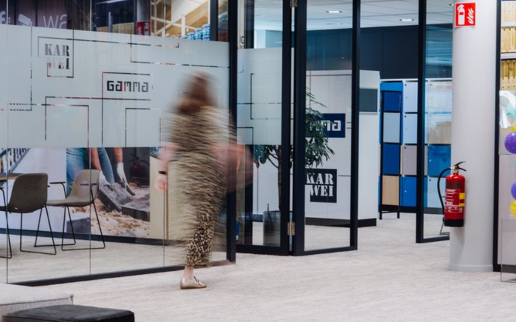 A photo of the interior of a modern looking office. The blurred shape of a woman is visible between meeting rooms.