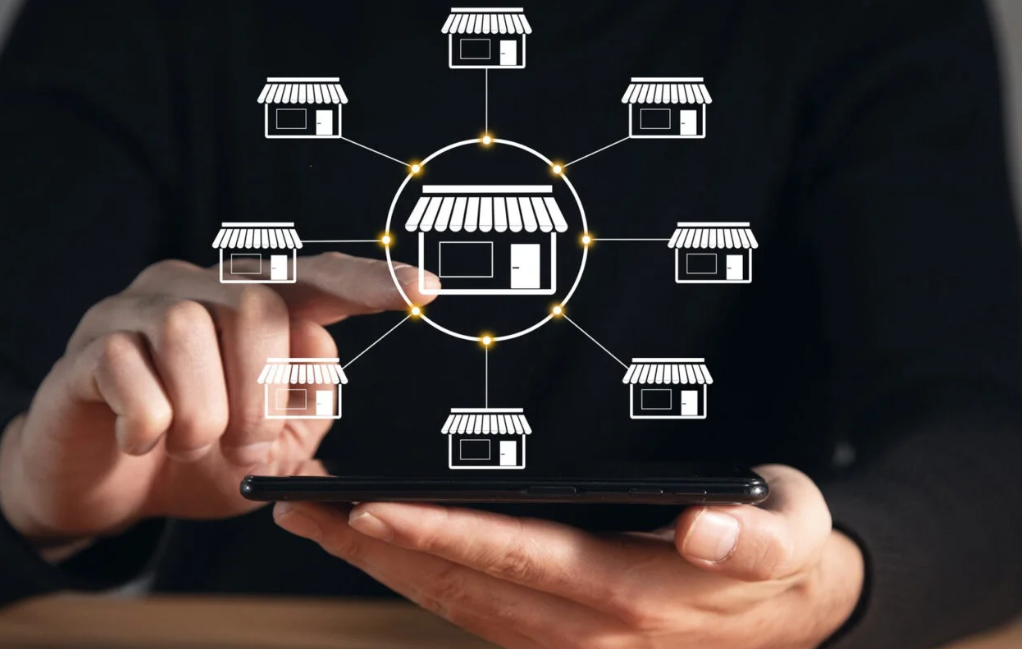 a pair of hands are interacting with a cellphone. White diagramatic pictures of stores are overlaid on top of the photo to suggest connected shopping or a retail hub.