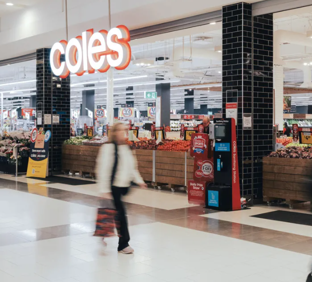A photo of the exterior of a Coles store. A blurred woman is in the foreground.