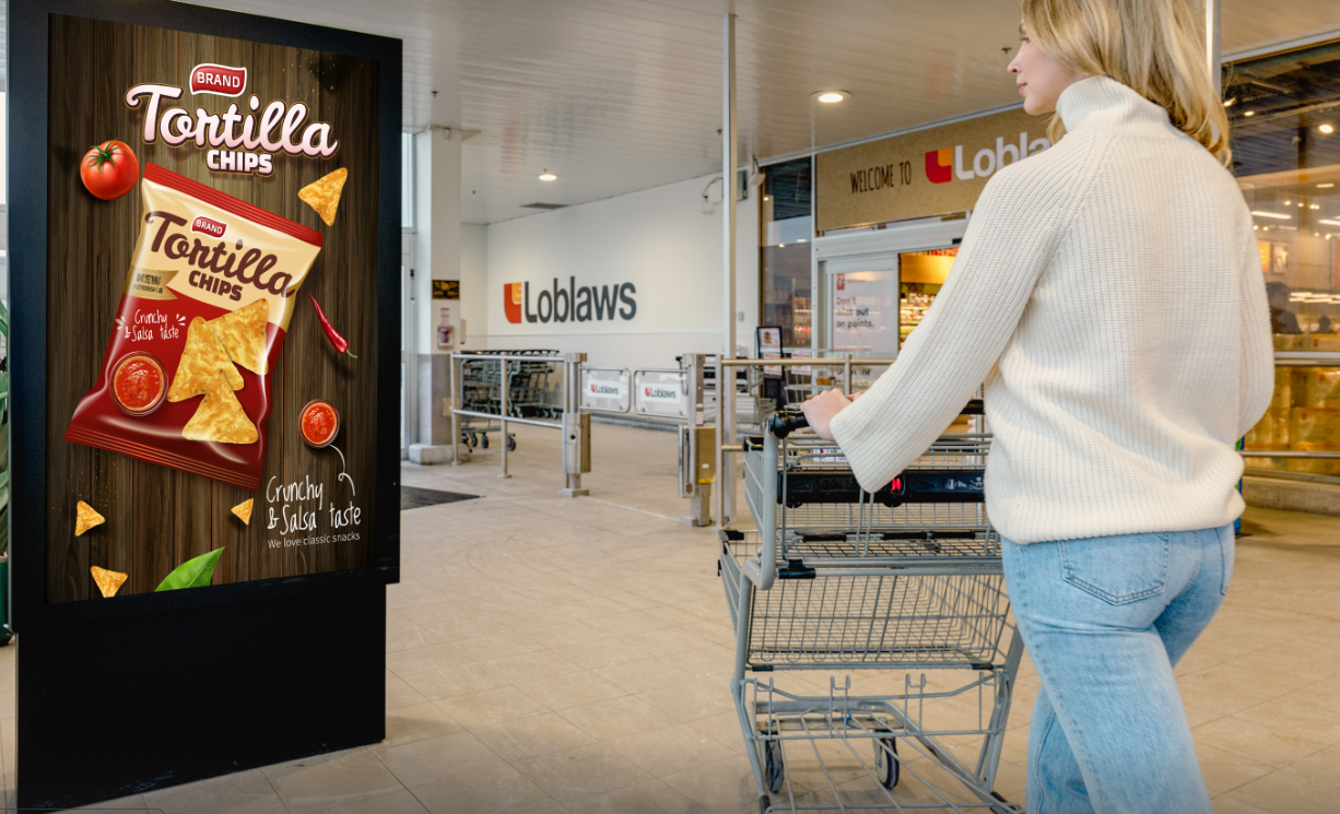 A shopper passes a shopping cart past a video screen in a loblaws store