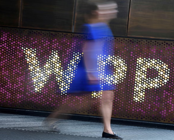 A photo of a woman who is blurry passing by the WPP logo).