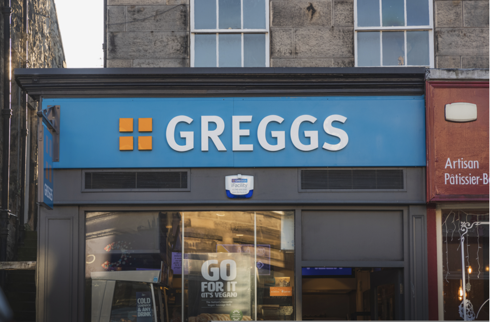 Photo is taken standing outside a Greggs store. The sign is blue.