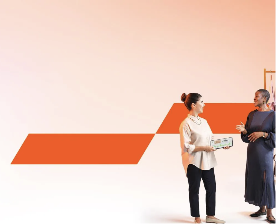 Two women standing in front of an orange logo for PwC