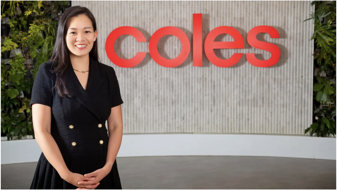 Tiffany Chen stands in front of the Coles logo. She is wearing a black dress.